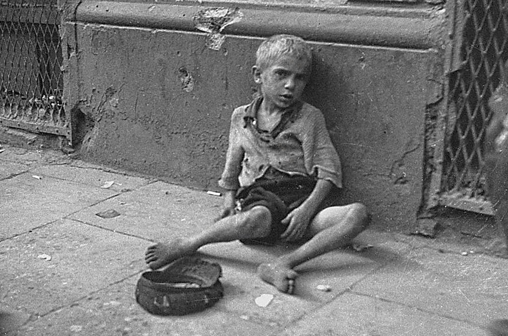 A starved boy begs on the sidewalk in the Warsaw ghetto.