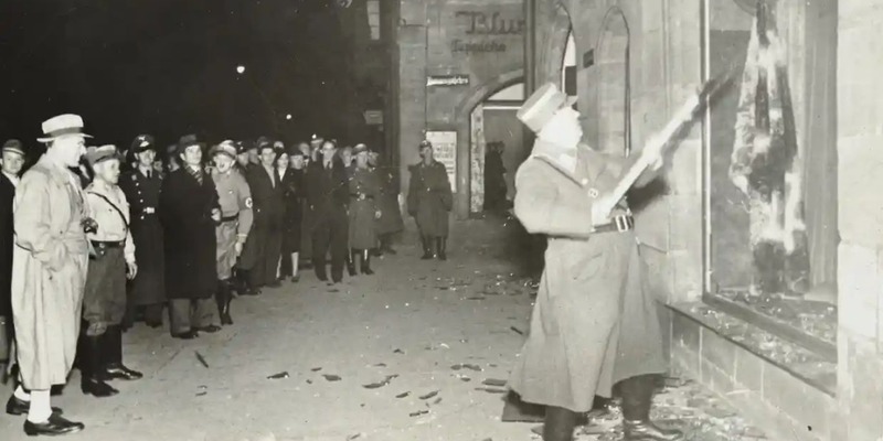 A shop window is smashed as onlookers watch during Kristallnacht.