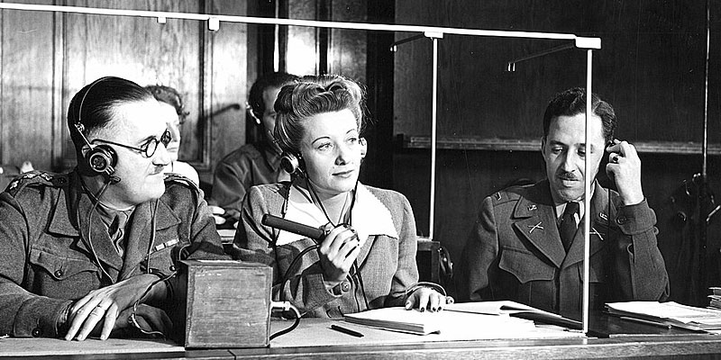 Simultaneous interpreters operating microphones and headphones inside a glass booth at the Nuremberg trials, circa 1945–1946.