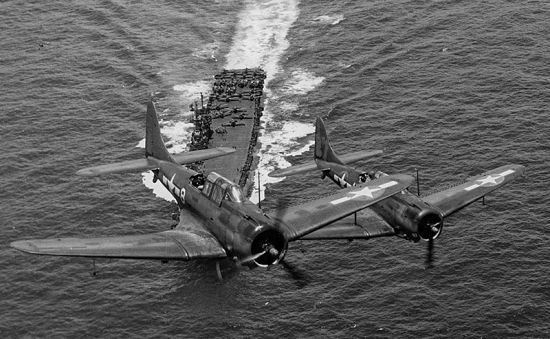 Douglas SBD Dauntless dive bombers fly over an American aircraft carrier during the Battle of Midway. The SBD played a decisive role in destroying four Japanese fleet carriers