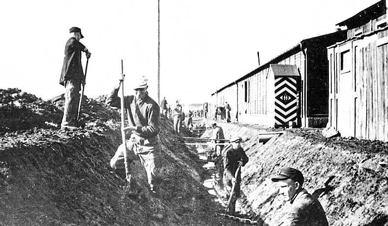 Slave labourers digging trenches with an SS booth in the background