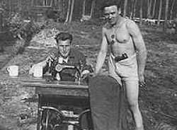 Germany 1945, March or April. Reichwald Forest. Ward sits at sewing machine (Gritzner model) obtained from a bombed out farm house. Standing is Junior Grey, from Western Canada. Ward was a part-time tailor.