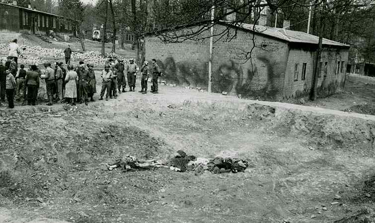 Corpses lie in a sunken mass grave outside a barrack of the Langenstein-Zwieberge concentration camp while survivors gather nearby.