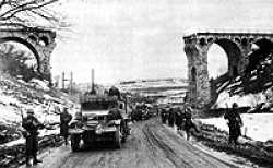 The 1st Battalion, 26th Infantry passing through the railway viaduct north of Bütgenbach, Belgium, on the Monschauer St. (N647) towards Bütgenbach. The railway viaduct was part of the line running from Losheim/Eifel (Germany) to Trois-Ponts, Belgium, and had been blown up by the retreating German troops.