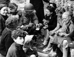 Commander Joseph P. Vaghi, USNR explains the worth of invasion money on June 19, 1944 to villagers at St. Laurent Sur Mer, Normandy.