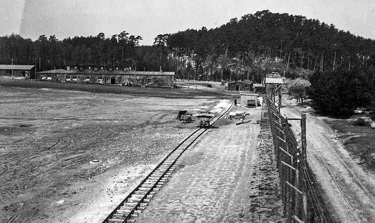 Area of the entrance to the camp train tracks, barbed wire electrical fence and barracks